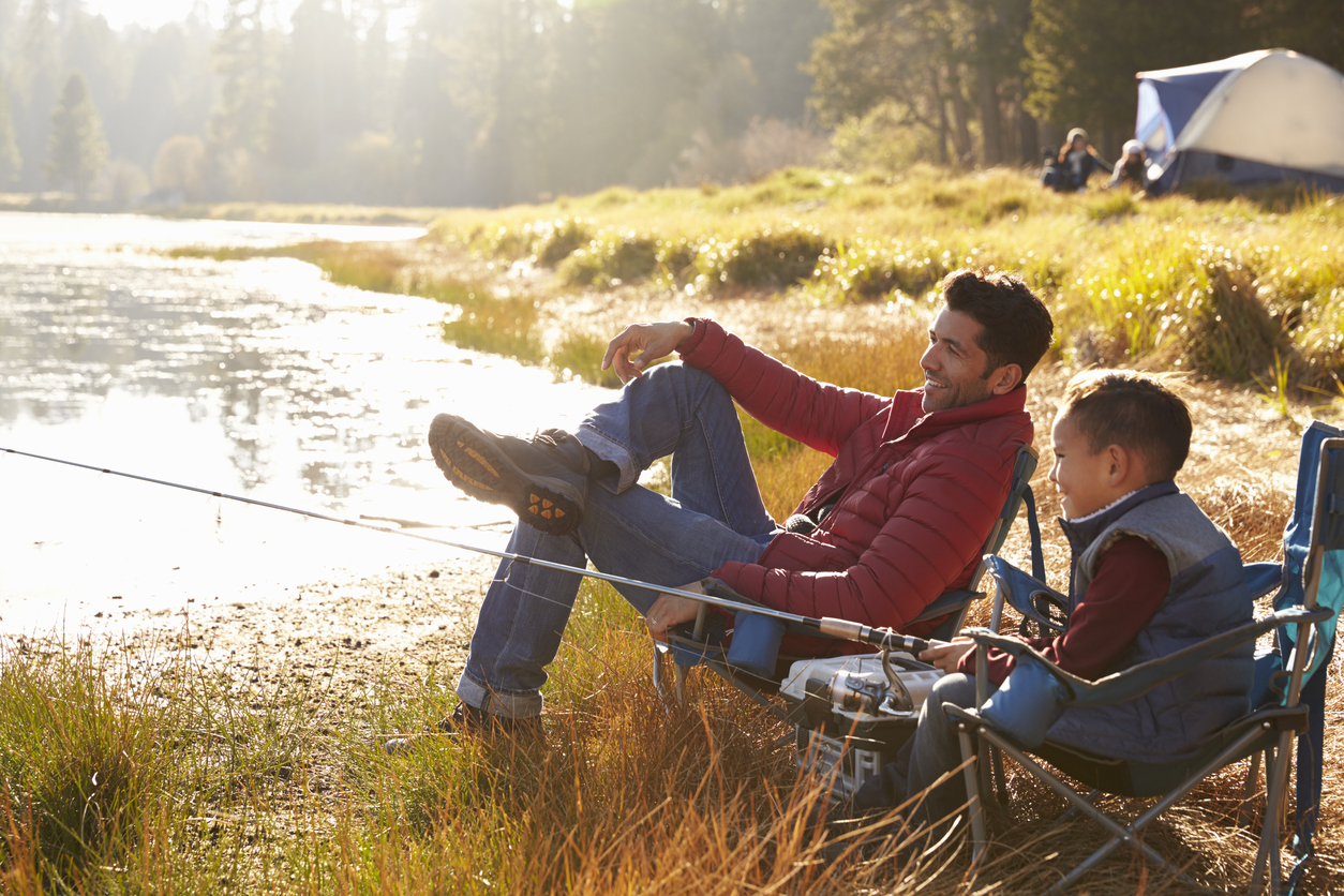 Father and son on a camping trip fishing by a lake.