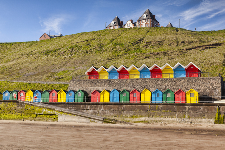 Rows of colorful beach huts on the promenade at Whitby Sands, Whitby, North Yorkshire, England, UK, on a beautiful sunny morning in spring.