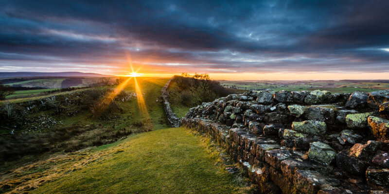 Sunset in Cumbria, United Kingdom. A stone wall is visible to the right and the skies are dark.