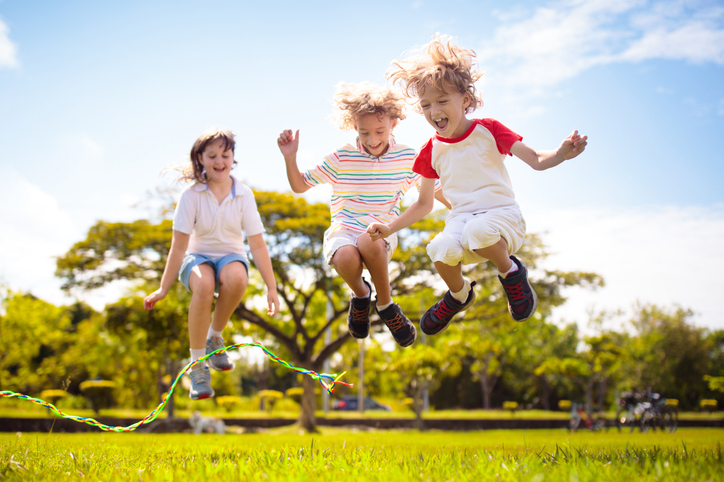 Happy kids play outdoor. Children skipping rope in sunny garden. Summer holiday fun. Group of school children playing in park playground. Healthy outdoors activity. Sport for child.