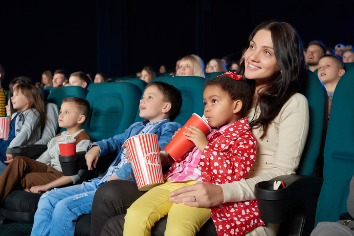 Young beautiful woman smiling holding her young daughter on the lap enjoying movie premiere at the cinema copyspace happiness living people leisure activity weekend togetherness concept.