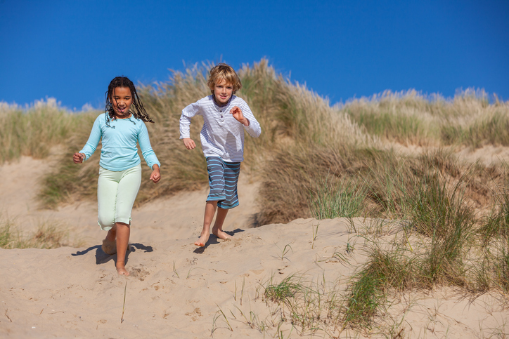 Two children, a blonde boy and a mixed race African American girl, having fun running racing in the dunes of a sandy beach