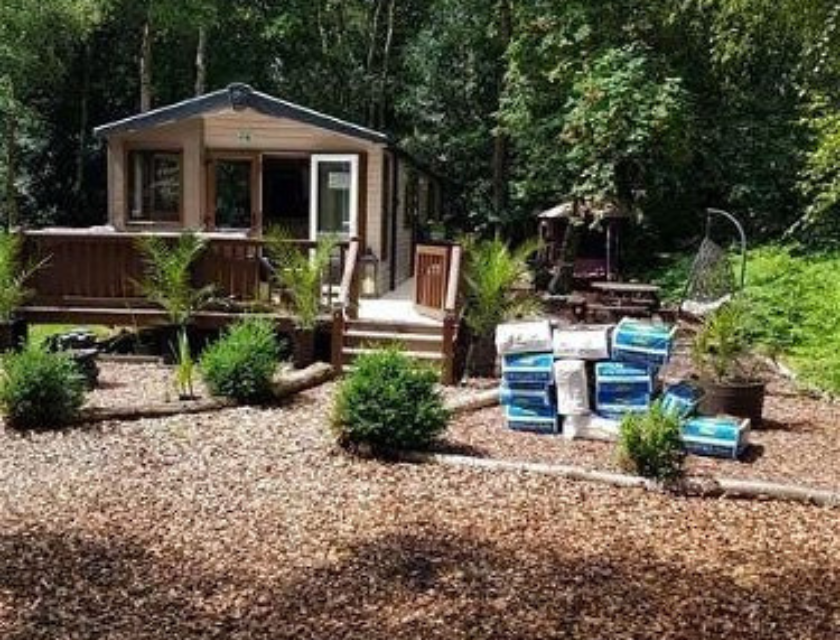 A static caravan set in a wooded area within Pinewoods Caravan Holiday Park in Norfolk. The caravan features a wooden deck and is surrounded by lush greenery and landscaped gardens. Ideal for nature lovers, this location offers easy access to scenic walking trails in Norfolk, perfect for exploring the natural beauty of the area.