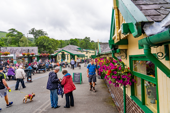 Llanberis, Wales, UK – July 2019. Tourists outside Llanberis train station waiting for a ride to the summit of Mount Snowdon on the Mount Snowdon Railway line. Find your Snowdonia accommodation here