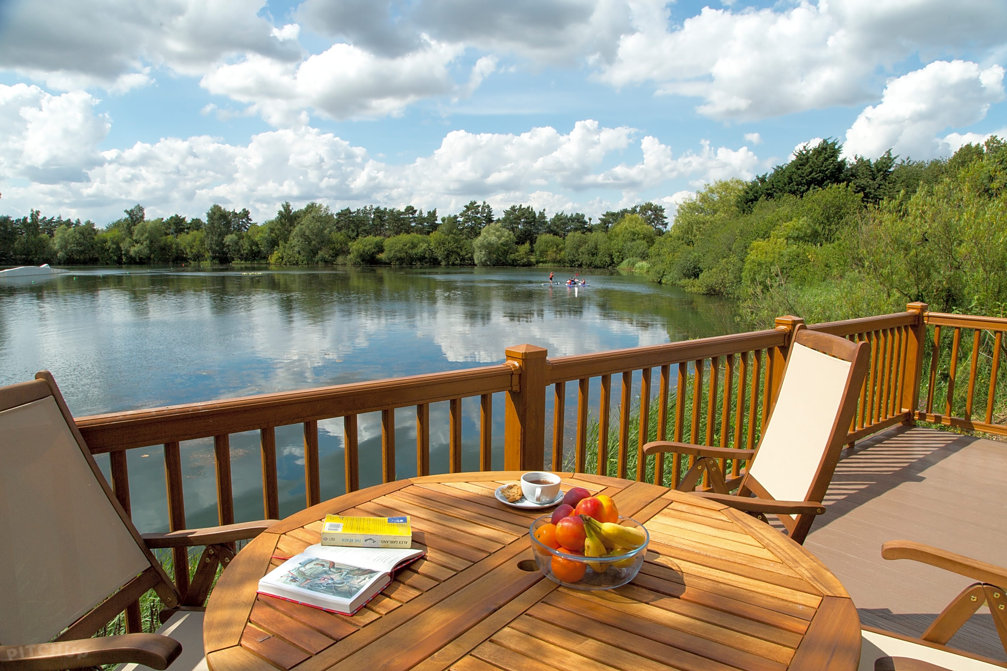 View from the patio of a static caravan in the Lake District, England. A wooden table with several items on it is visible. Two wooden chairs are also visible at either side of table.