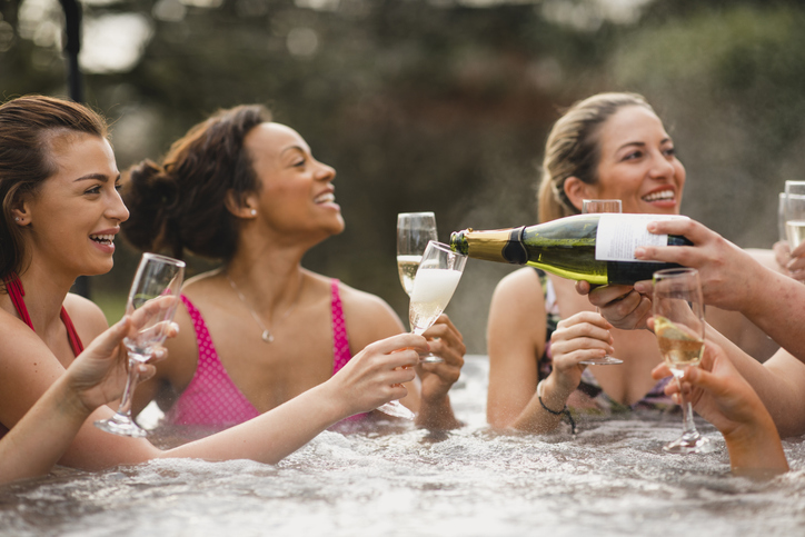 Small group of female friends socialising and relaxing in the hot tub on a weekend away. They are celebrating with a glass of champagne.