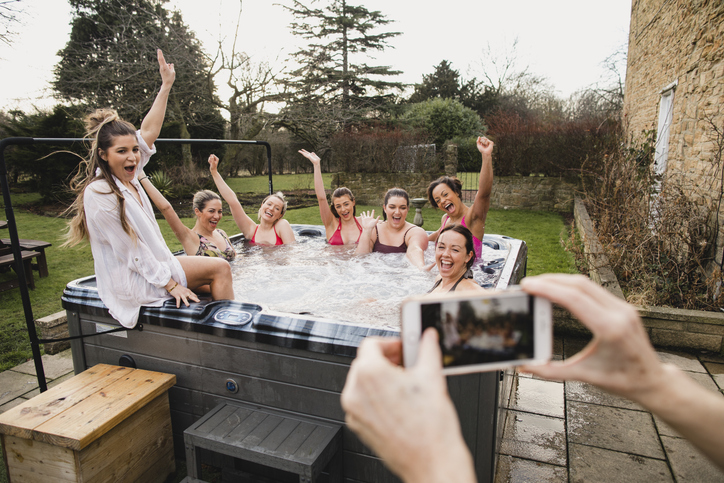 Small group of female friends relaxing and celebrating in a hot tub. They are all looking towards their friend who is taking a group photo of them.