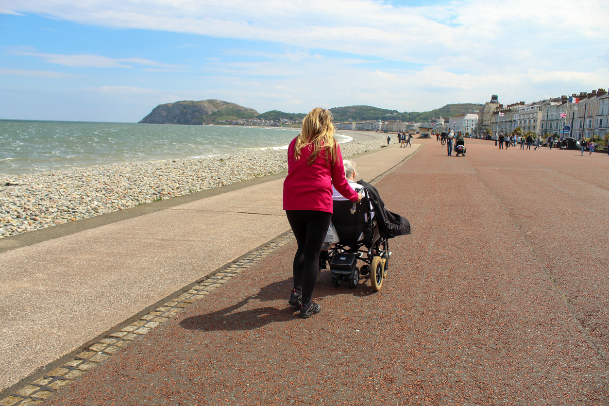 A middle aged woman pushes her elderly and disabled mother in a Wheelchair along the Promenade at Llandudno, Wales.