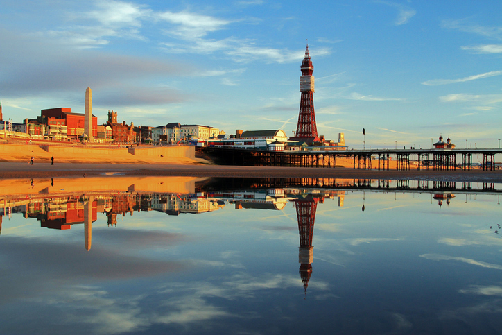 British beaches of the west coast. A Fylde Coast Golden Hour Reflection of Blackpool Tower and North Pier on a calm still early evening glow. Blackpool beach shoreline is visible.