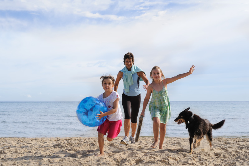 Woman in her 50s with two children and a dog running towards the camera, sea and beach surroundings.