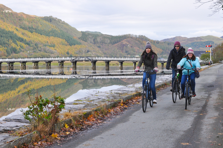 Dolgellau, Wales, UK - October 30th, 2018: Three cyclists on the disused railway track on the edge of the spectacular Mawddach estuary which links Dolgellau and Barmouth.