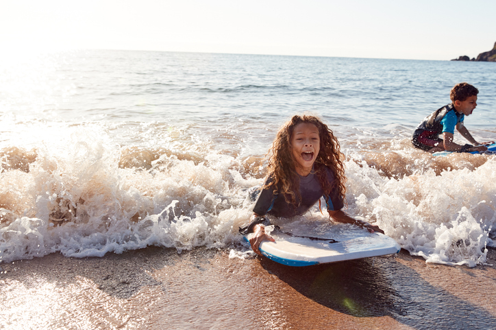 Two Children Wearing Wetsuits Playing In Sea With Bodyboards On  Summer Beach Vacation