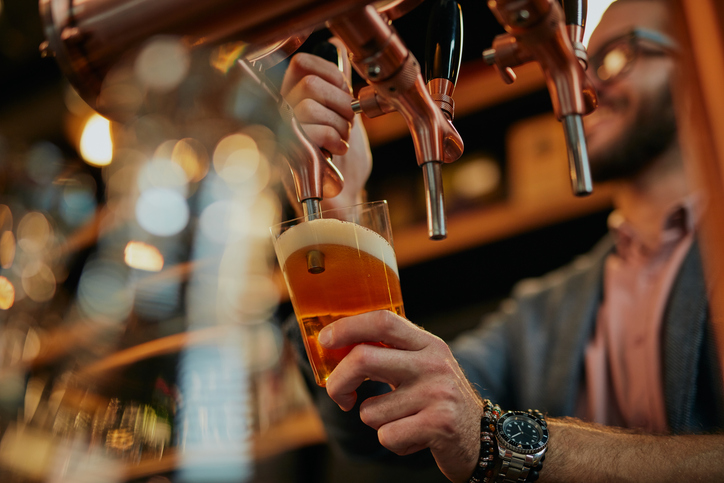 Tattooed caucasian barman pouring beer while standing.