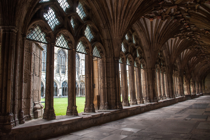 Interior corridor with windows, columns and high ceilings in the Cnterbury Cathedral building. Courtyard with green landscaped grass.