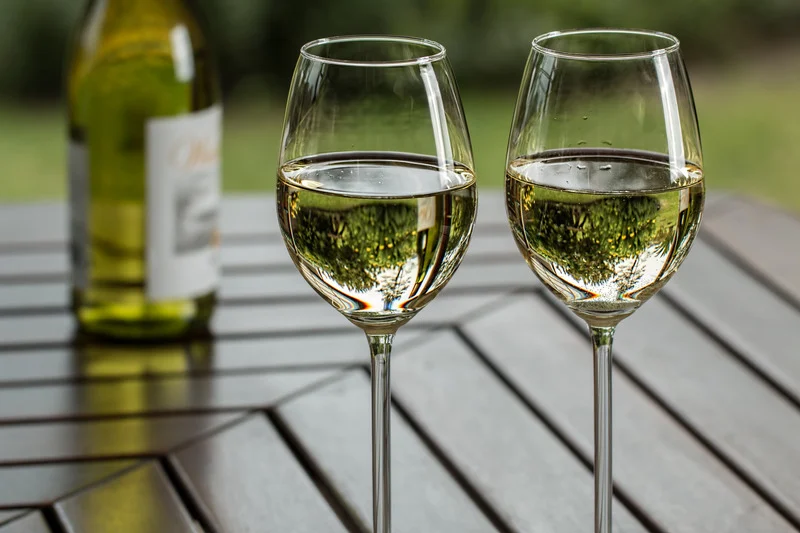 Two wine glasses half full of win on a wooden table with the bottle out of focus behind