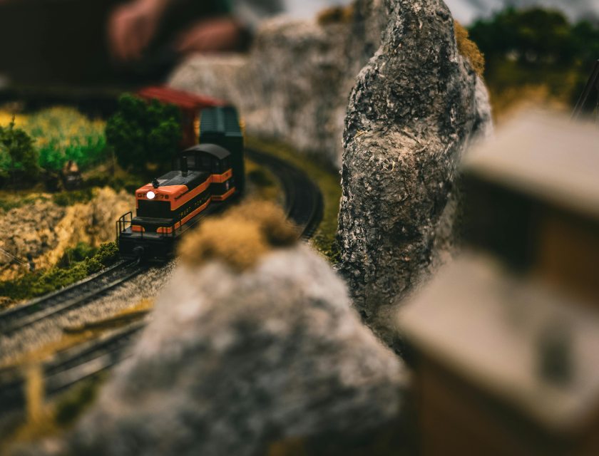 A detailed model train set with a miniature train winding around rocky terrain and green scenery.