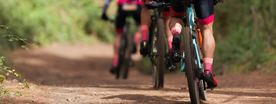 Close-up of cyclists riding on a dirt trail through a forest, showcasing their legs and bicycles.