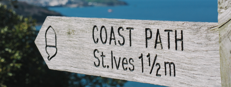 Find beautiful cycling trails in Cornwall. A close up of a sign pointing to the Coast Path St Ives.