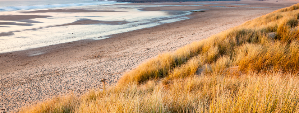 Golden sand dunes overlooking a wide, empty beach at low tide, with shallow water reflecting.