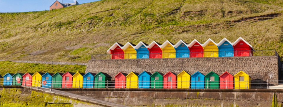 Rows of colorful beach huts on the promenade at Whitby Sands, Yorkshire, Whitby Beach, England, UK, on a beautiful sunny morning in spring.