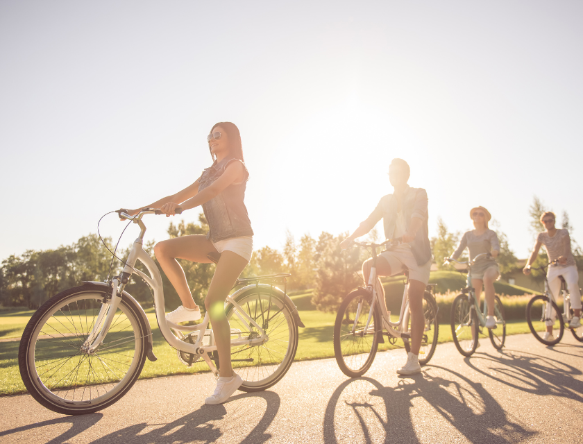 A group of cyclists, including both adults and children, enjoy a sunny ride on a paved path through a park The bright sunlight and open space emphasize the leisurely and joyful atmosphere of cycling in scenic outdoor settings