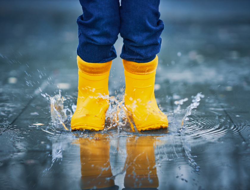 A child wearing bright yellow rain boots splashing in a puddle, highlighting the joy of playing outdoors even on a rainy day.