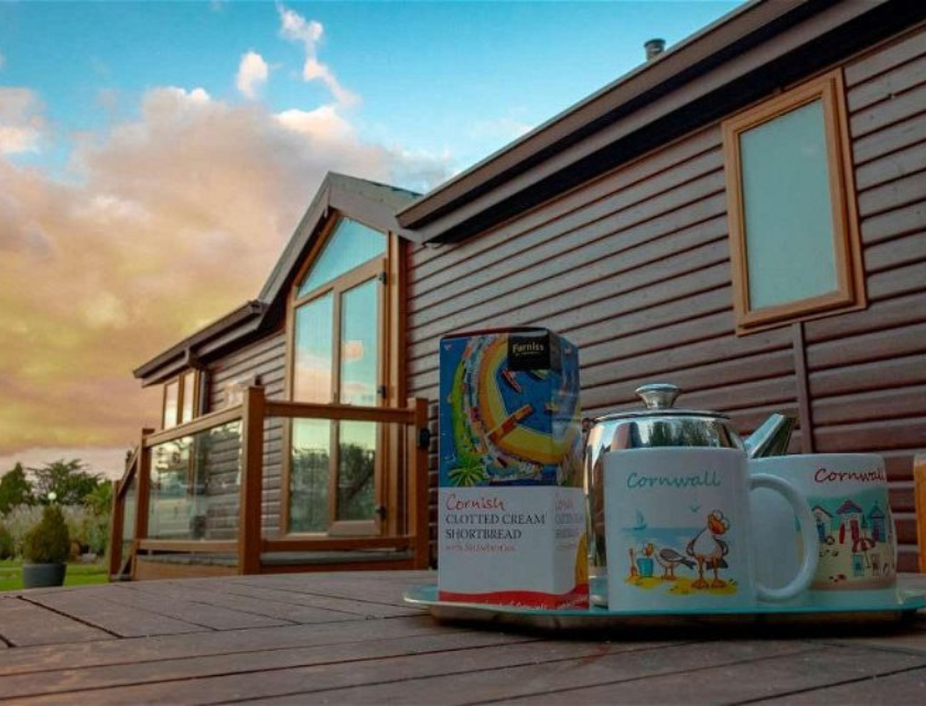 A cozy lodge with a tray of Cornish-themed tea and shortbread on the deck, reflecting the relaxing and scenic accommodations available at holiday parks near Mevagissey, such as Meadow Lakes Holiday Park.