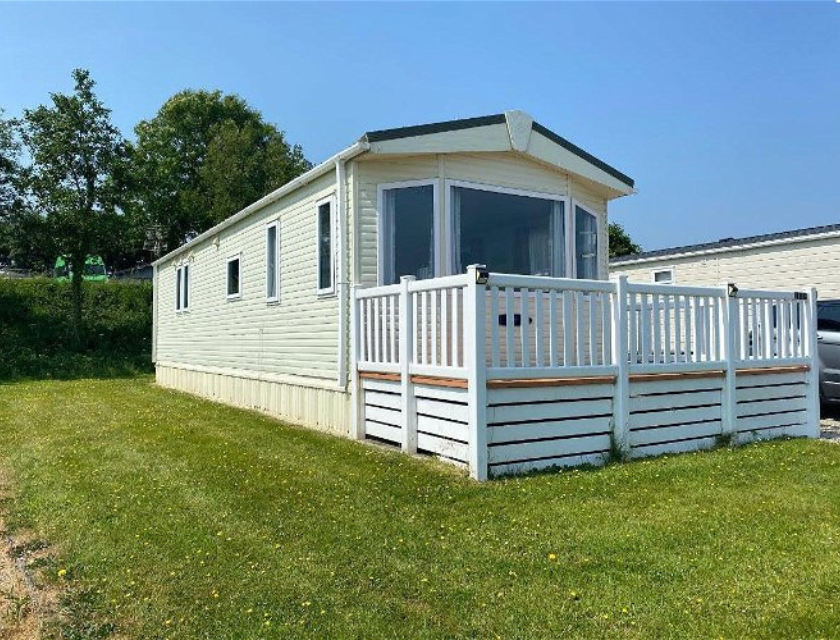 A static caravan with a spacious deck, located in a grassy area under clear blue skies, showcasing the comfortable and family-friendly accommodations at places like Par Sands Holiday Park near Mevagissey.