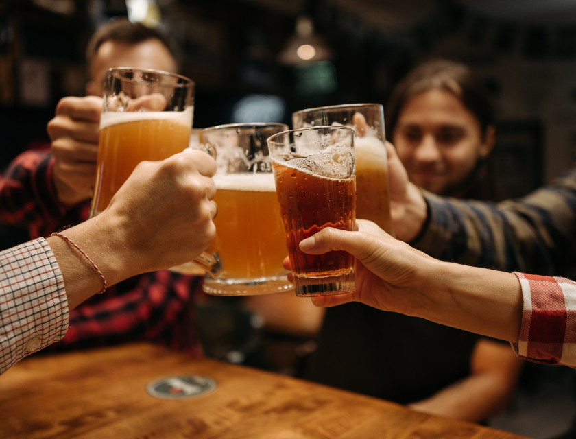 The Mulberry is a popular bar near Conwy Morfa Beach. Close up shot of four people toasting beers with four clear beer glasses. The glasses are in focus and the people in the background are out of focus.