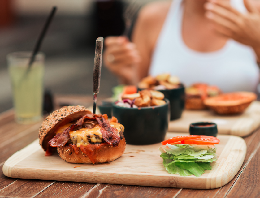 Close-up of a bacon cheeseburger served on a wooden platter. Lettuce and other accompaniments on the side.