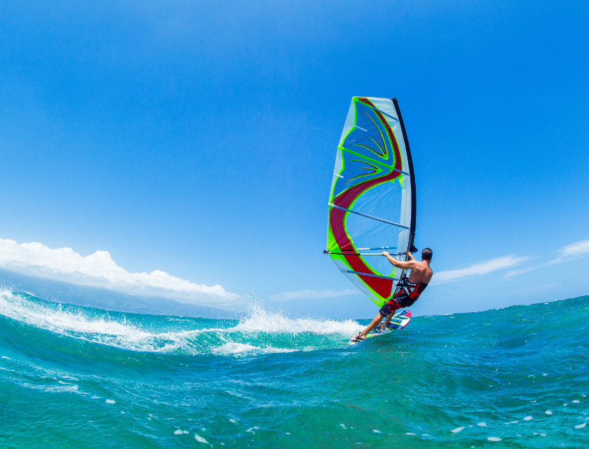 Man windsurfing in the ocean on a sunny day. Crystal clear blue waters below and a pristine bright blue sky above.