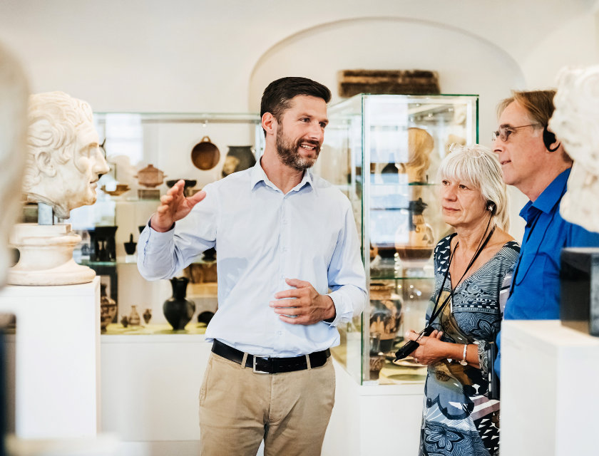 Museum guide talking to an older couple (man & woman) in a museum. The image is brightly lit. The Tate is a popular rainy day thing to do in Cornwall for families and solo travellers.