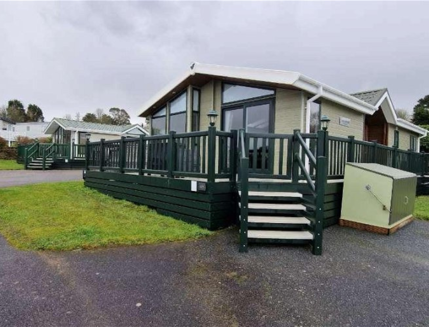 Static caravan with stairs leading up to it. There is a small patch of grass at either side. The sky is grey.