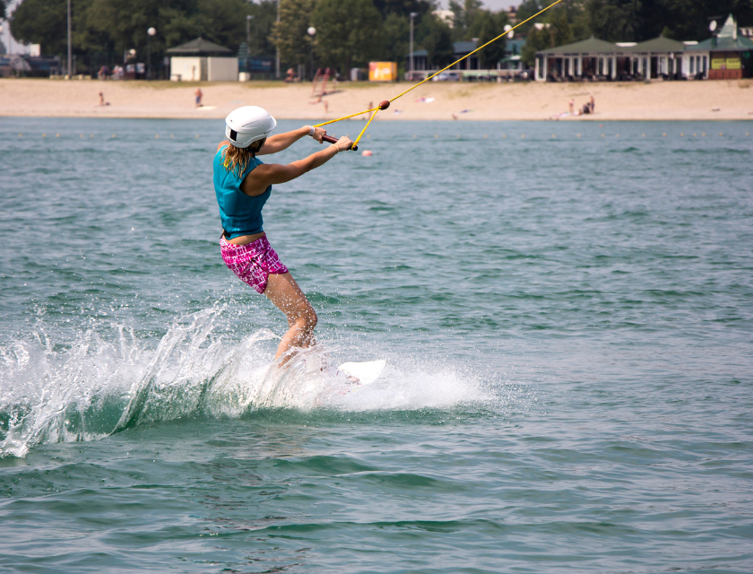 Shot from behind. Woman wearing a cap while kitesurfing with shoreline in the background. 