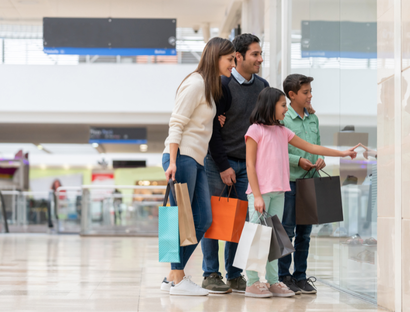 A family looking window shopping at a mall while all holding shopping bags of different colours.