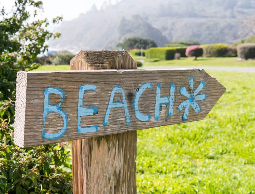 A wooden signpost pointing towards a beach, symbolizing the nearby picturesque beaches such as Porthmellon and Gorran Haven near Mevagissey.