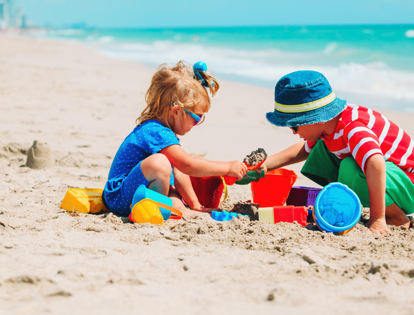 Two young children playing with colorful toys on a sandy beach, representing family-friendly beach activities available near Mevagissey.