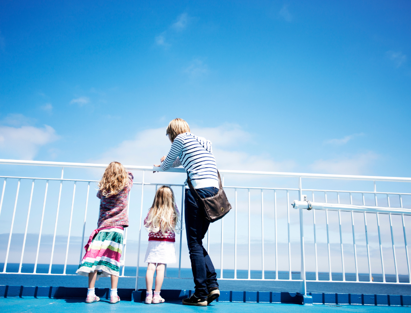 Woman and two children (two young girls) looking over a white fence. The light blue sky has several visible clouds. 