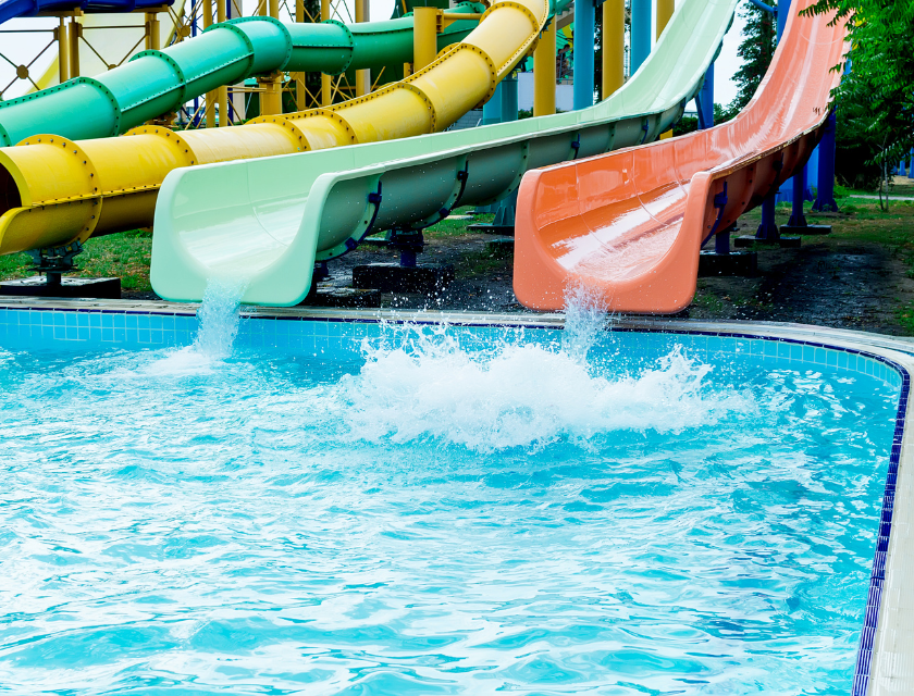 Water splashes into a pool at the end of several colorful water slides, capturing the fun and excitement of a day spent at a water park.