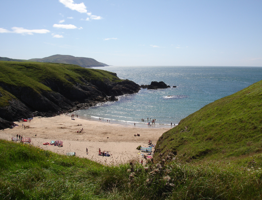 North Wales is a peaceful location for relaxation and family outings. Image shows a hidden beach nestled between green hills, with soft golden sands meeting the gentle waves of the sea. 