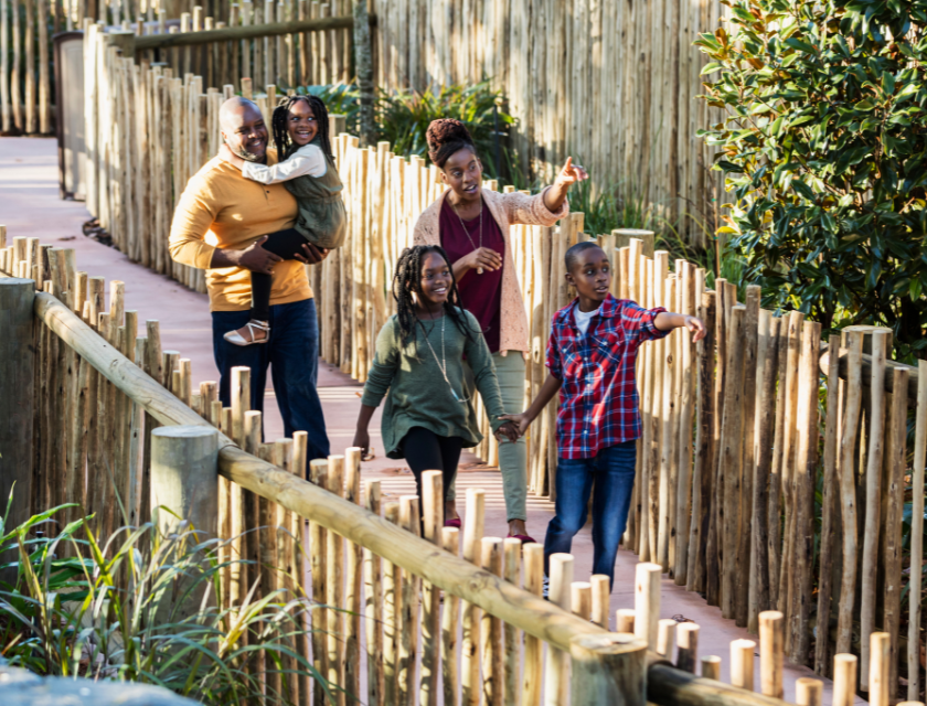 Wildlife in North Wales is a must-visit for families exploring wildlife attractions. Image shows a joyful family walking through a zoo, surrounded by wooden fencing and greenery. 