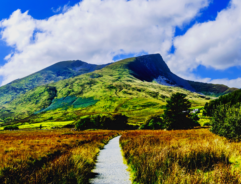 A scenic pathway leading through lush greenery toward a towering mountain peak under a partly cloudy sky, perfect for hiking and outdoor exploration.