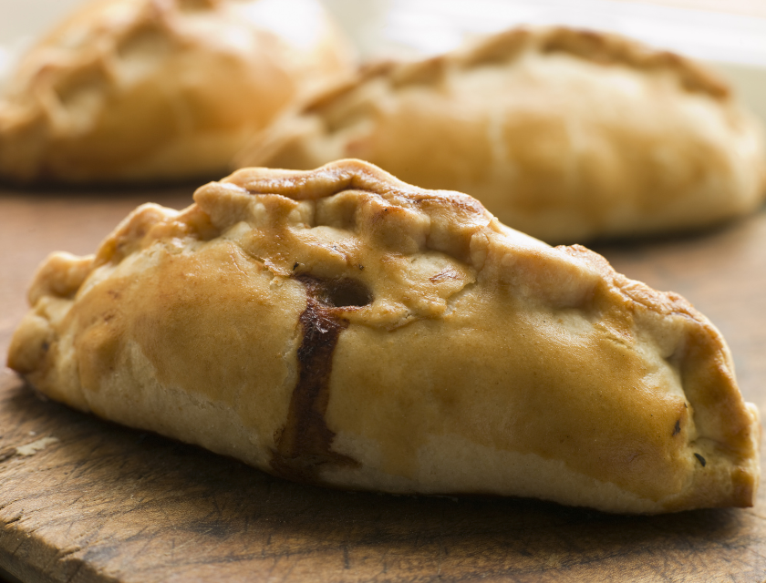 Fudgies Bakehouse near Woolacombe Beach is a favourite with tourists. A close-up of freshly baked Cornish pasties, golden brown with crimped edges, resting on a wooden surface.