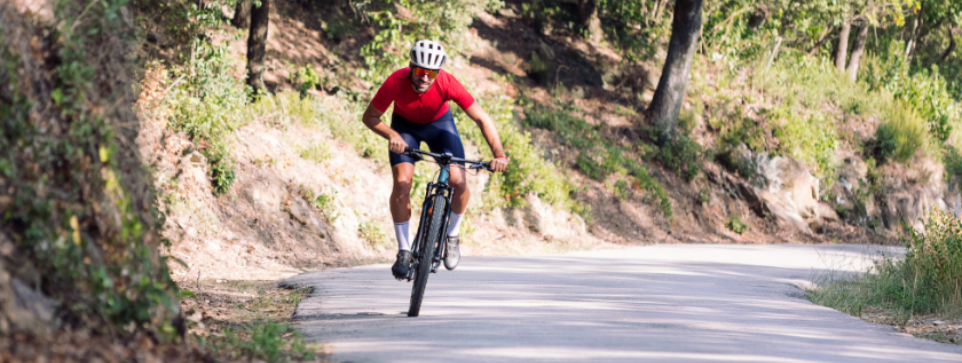 There is opportunity to challenge yourself when cycling the hills of Yorkshire.. Cyclist in red shirt riding downhill on a winding road through the woods