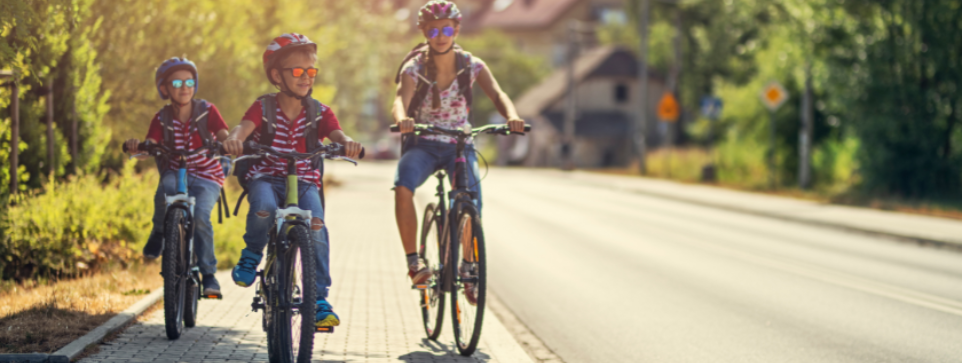 There are plenty of family friendly cycling trails in Yorkshire | Image shows a parent and two children cycling together on a sunny day along a quiet road.