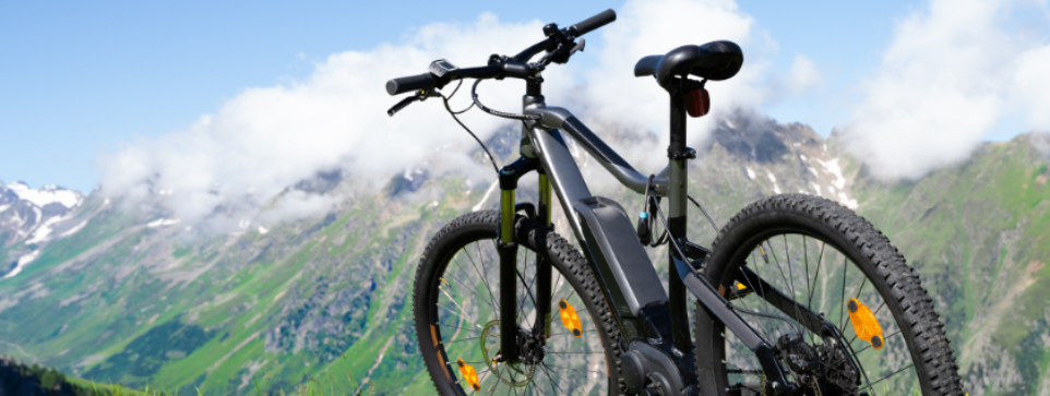 A black mountain bike standing with no rider. Scenic mountainous background , and a rugged terrain. 
Partly cloudy sky.