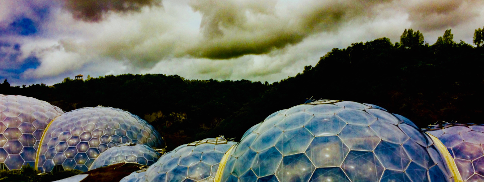 Several large, clear geo domes set against a backdrop of dark trees and cloudy skies. Part of a futuristic-looking structure in a garden.