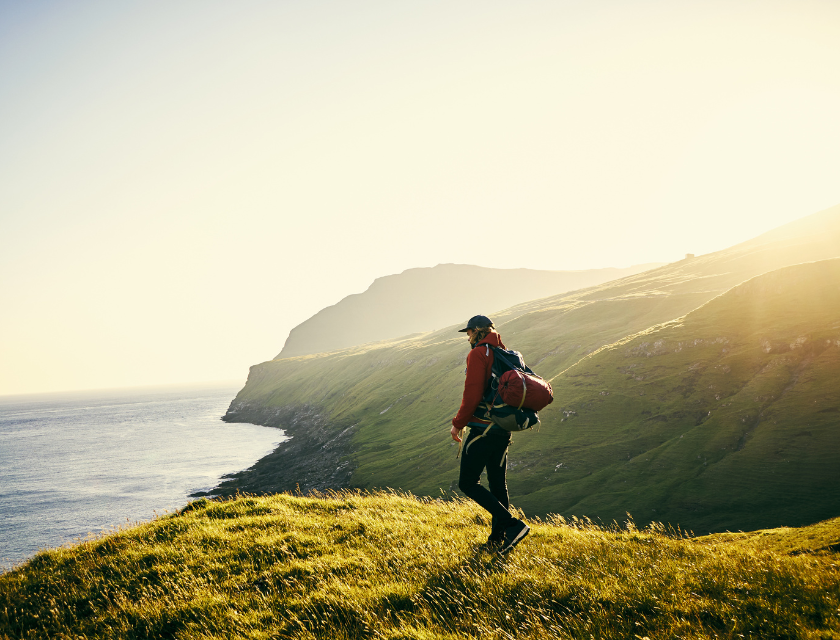 A solo hiker walking along a grassy cliffside with the ocean in the background, depicting the scenic and tranquil coastal walks in Torquay.