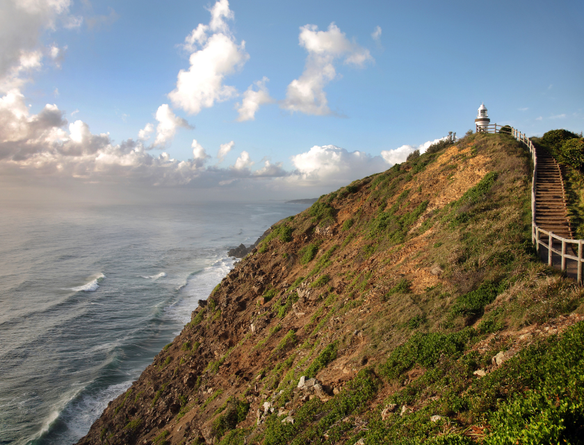 A coastal path along a rugged cliff with a lighthouse perched on top, overlooking the ocean. This represents the coastal walks in Torquay, where walkers can experience breathtaking sea views.