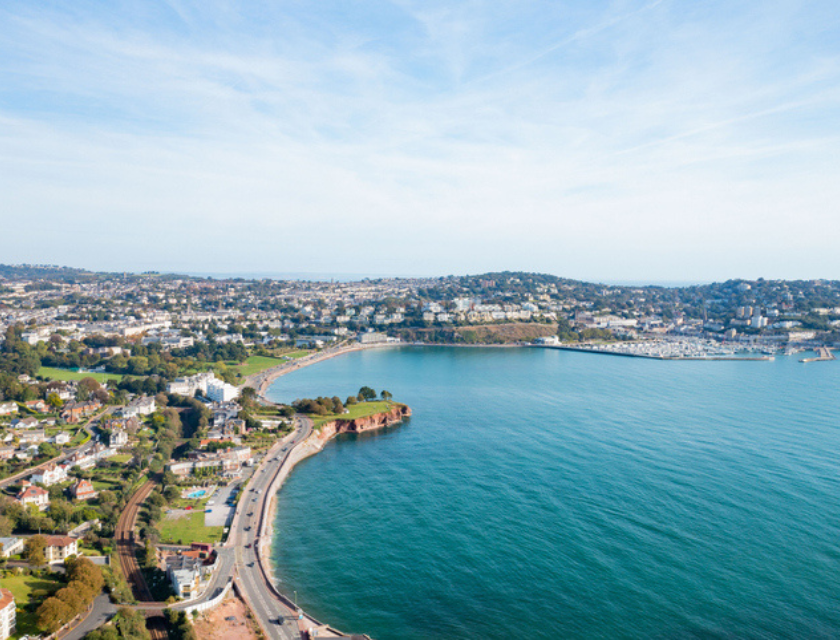 An aerial view looking over Torquay Sea Front in South Devon. Shot on a sunny day with blue ocean and the tide in.